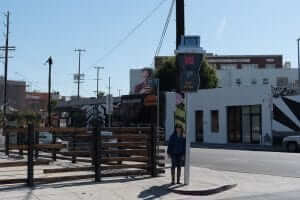 A person is standing on a sidewalk next to a street sign.