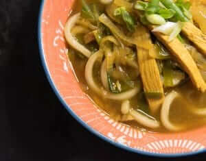 A bowl of curry udon with chicken and green onions.