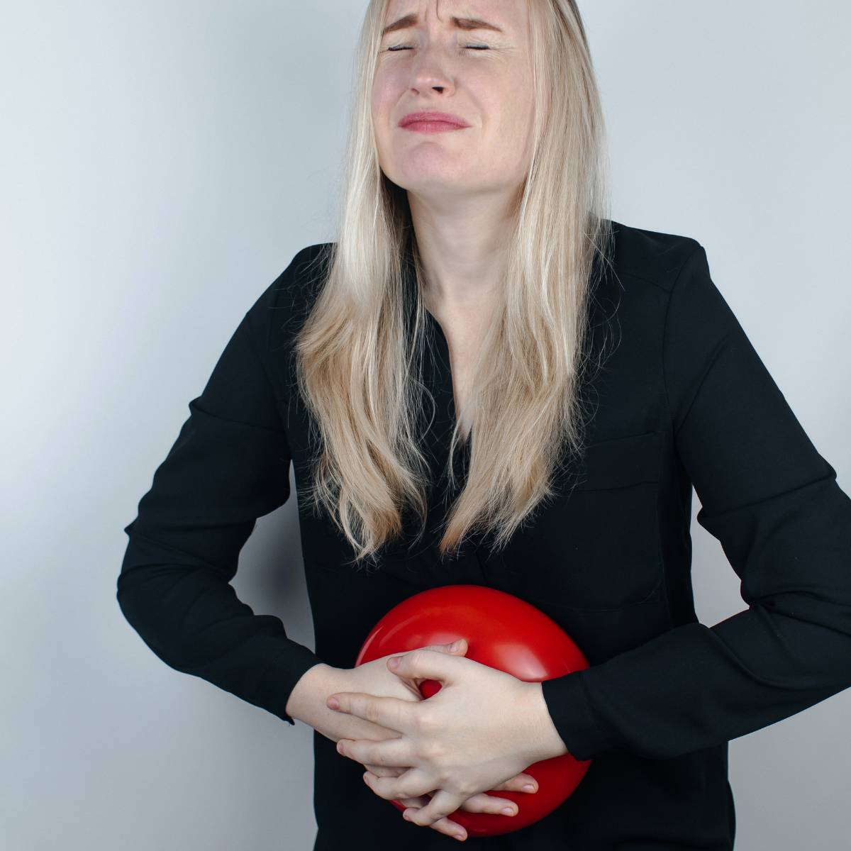 Woman wearing black cloth and holding a red balloon having a gassy tummy