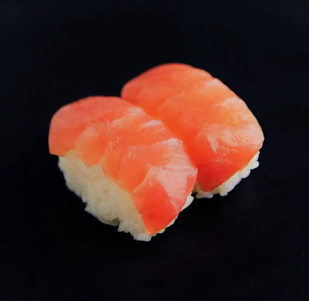 Sushi grade salmon sushi on a black surface.