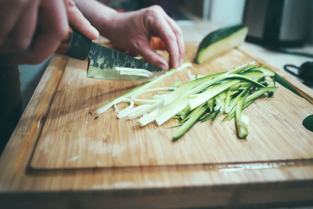 A person preparing zucchini on a wooden cutting board.