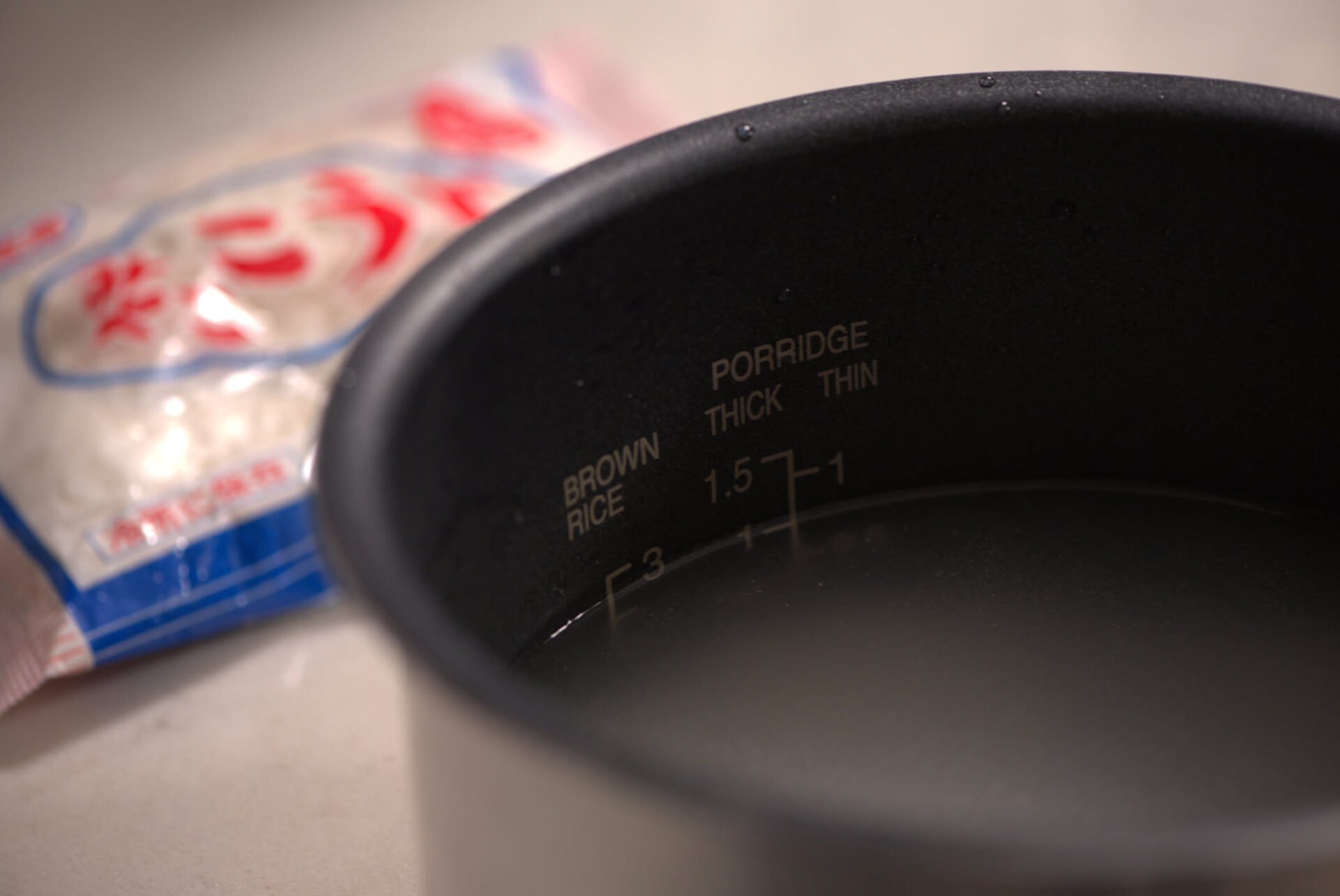 Rice cooker inner pot showing the brown rice fill line beside a bag of Japanese rice