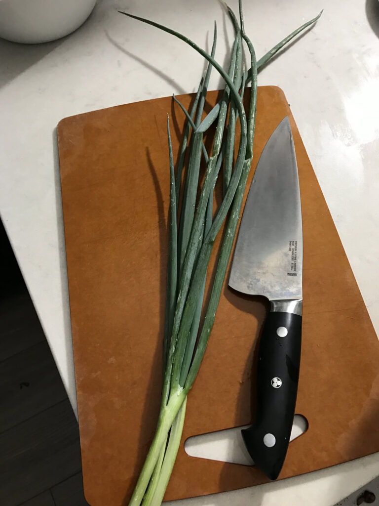 Japanese kitchen knife and scallions on a wooden cutting board