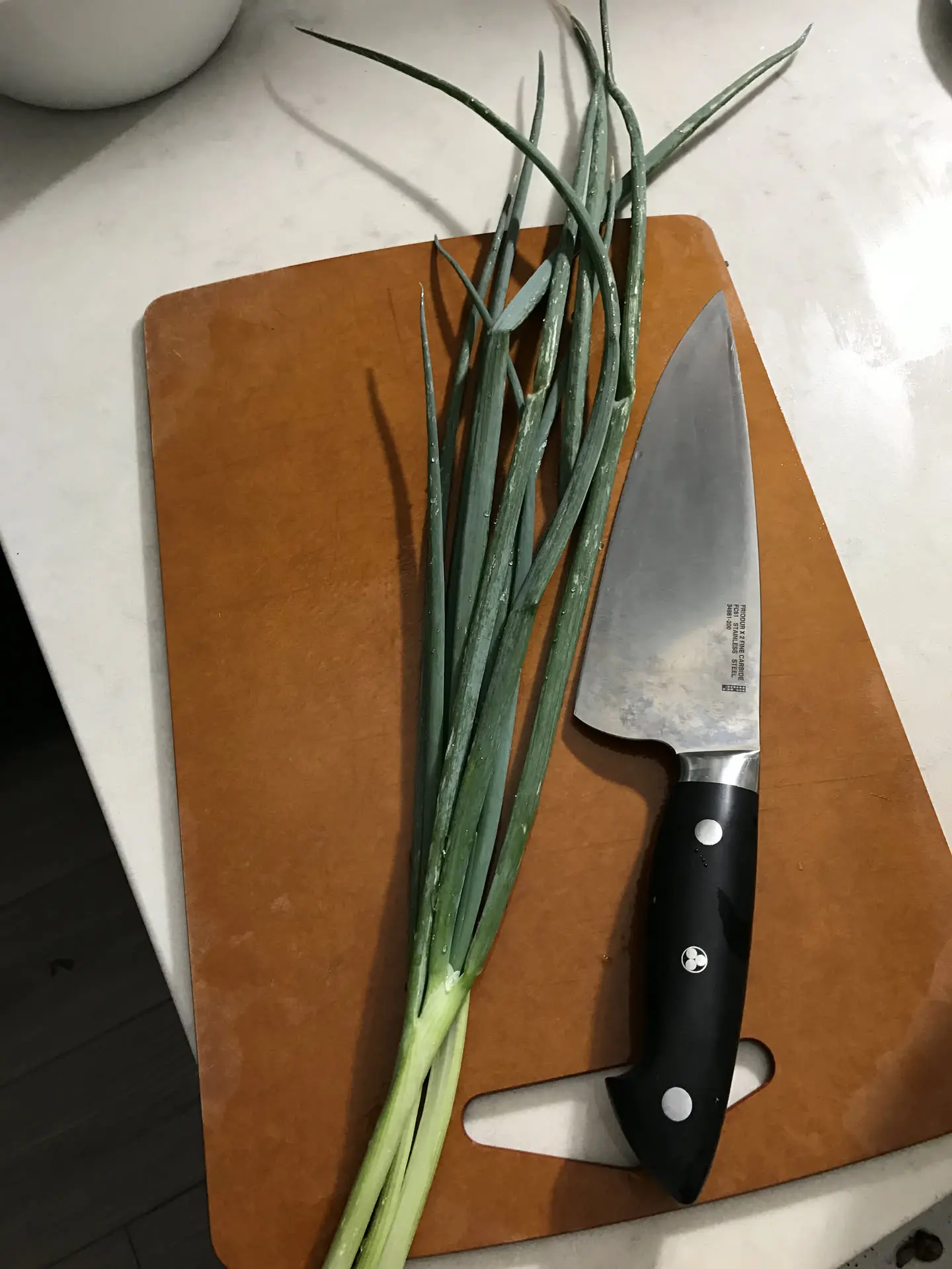 Japanese kitchen knife and scallions on a wooden cutting board
